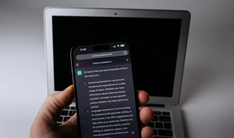 Smartphone showing a ChatGPT conversation in front of a laptop.